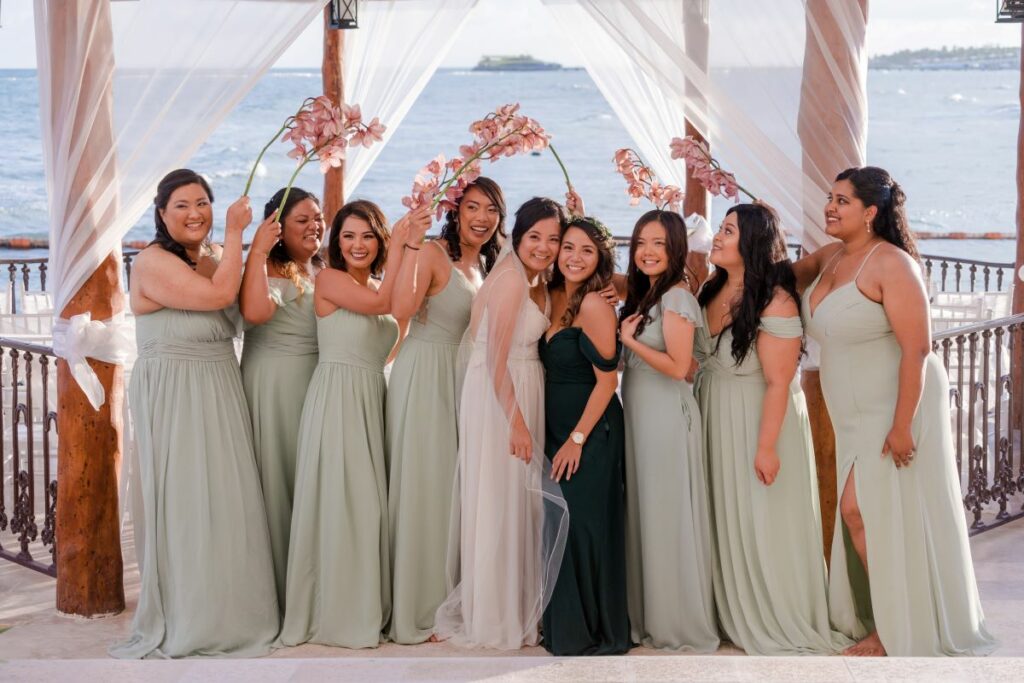 Bridesmaids dressed in light green holding pink flowers and bride posing at the ocean front gazebo