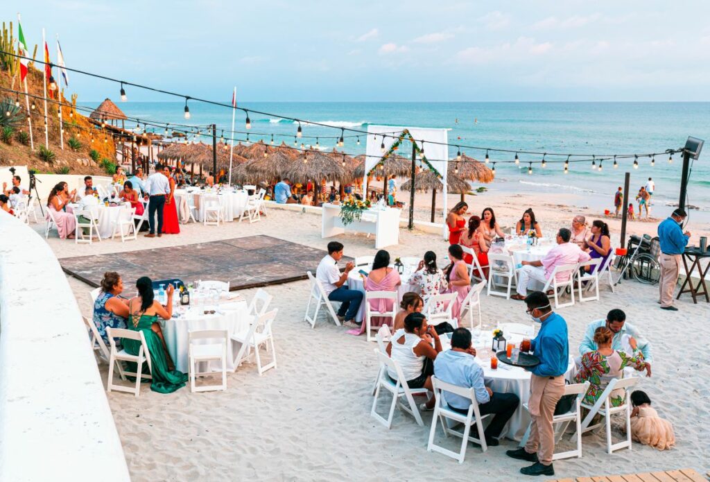 Beach wedding set up with round tables and a dance floor with guests seated