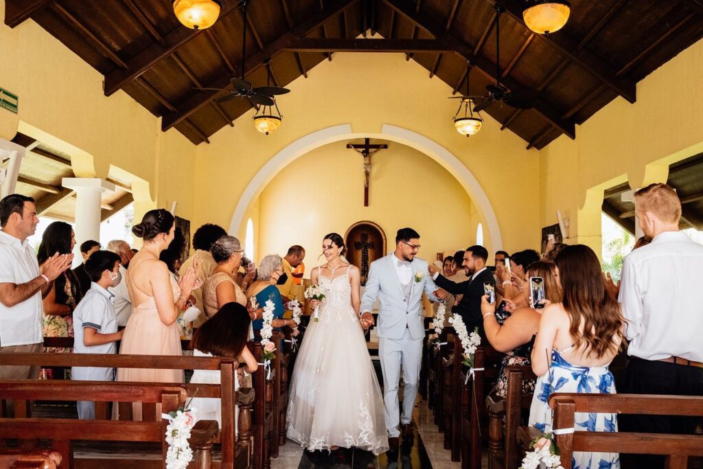 A just married couple leaving the ceremony at the catholic chapel while guests clap