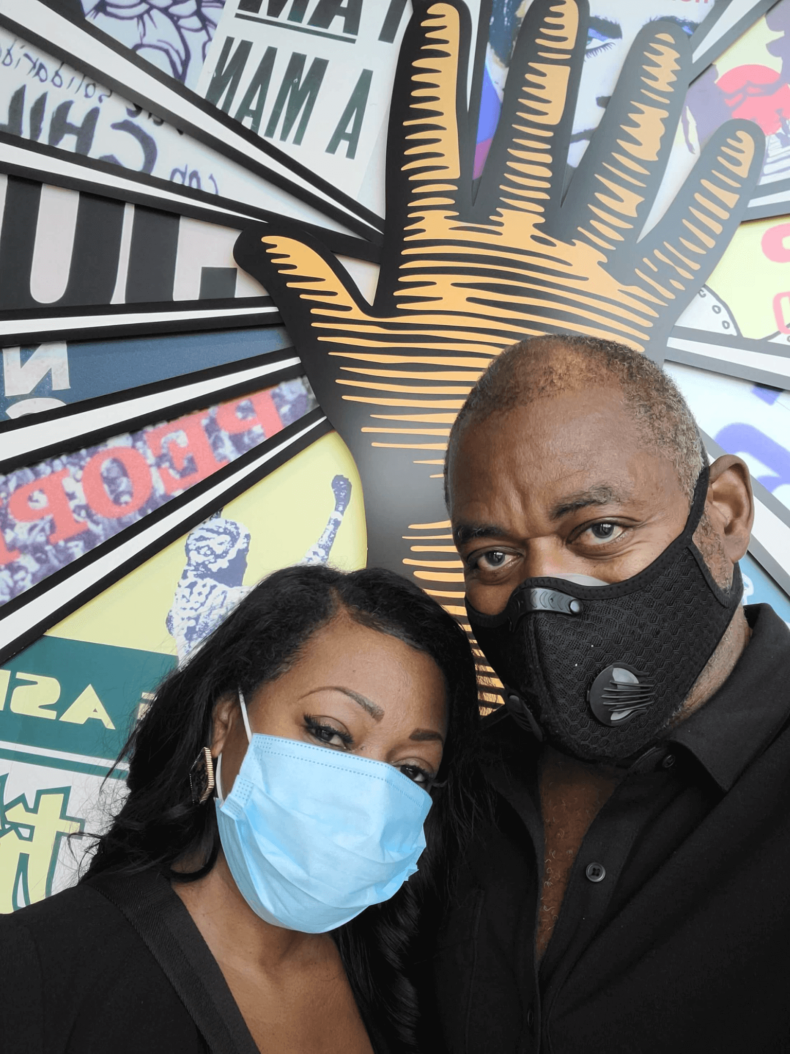 Couple wearing face masks taking a selfie in front of a mural