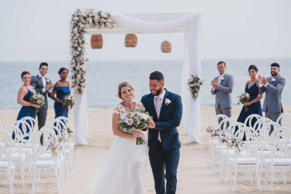 Just married couple walking down the aisle and a gazebo with flowers on the beach