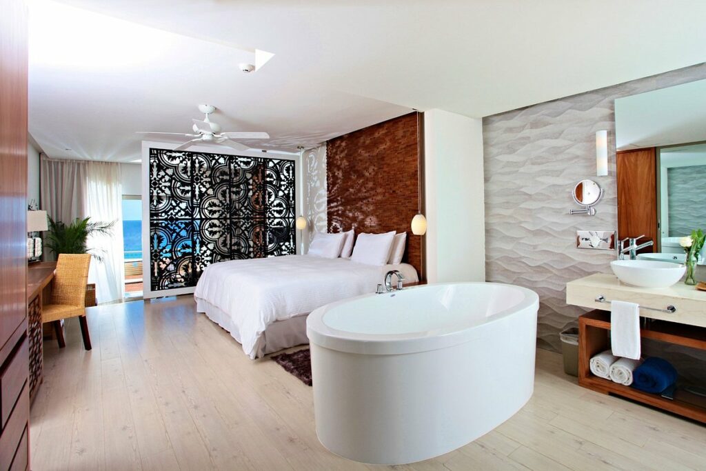 Hotel suite with modern decor, a king size bed and a hot tube in the bathroom, ocean view from the balcony