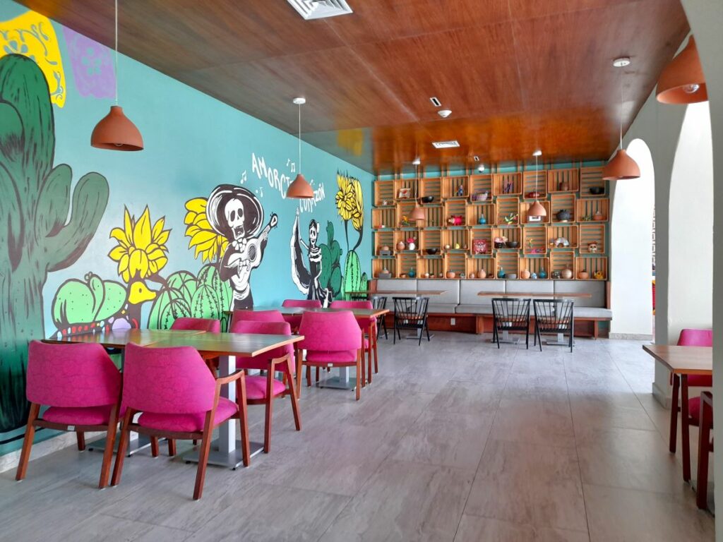 mexican restaurant with bring pink chairs and a mural painting with singing mexican skulls