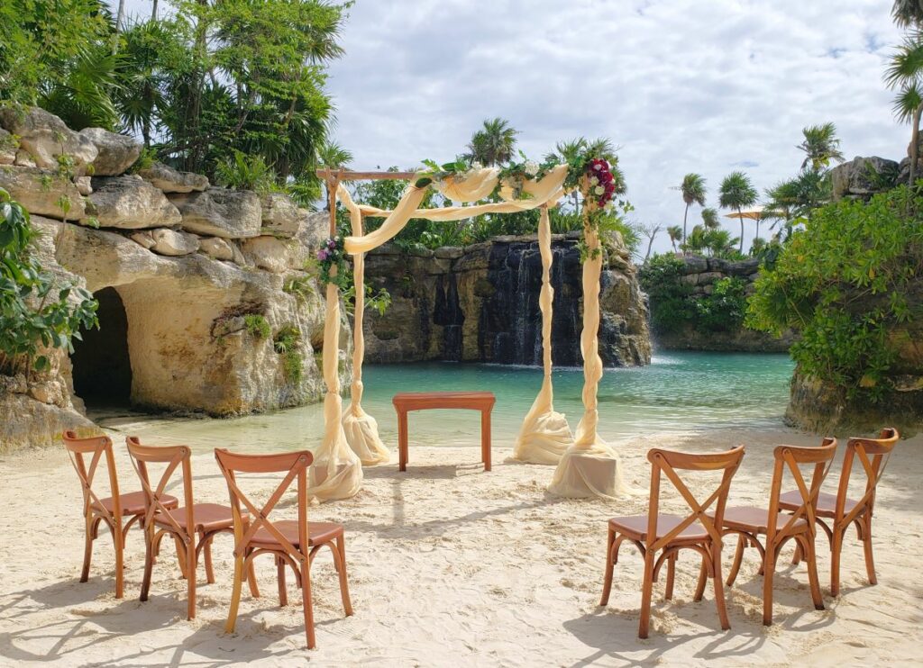 Destination Wedding gazebo on the beach with white drapes with flowers and a few wooden chairs at hotel xcaret