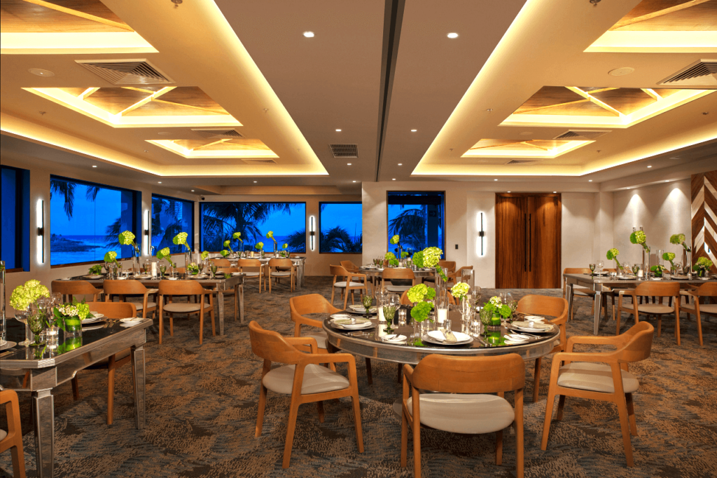 Modern ballroom with large windows overlooking the ocean, wooden furniture and flower arrangements at the tables