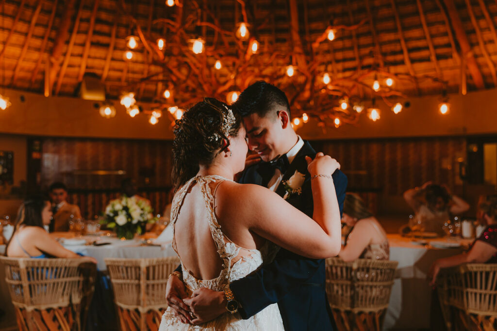 A wedding couple holding each other on their first dance in a beautiful ballroom filled with lights
