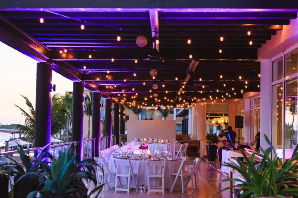 wedding reception set up on an ocean front terrace, with hanging lanterns and white round tables