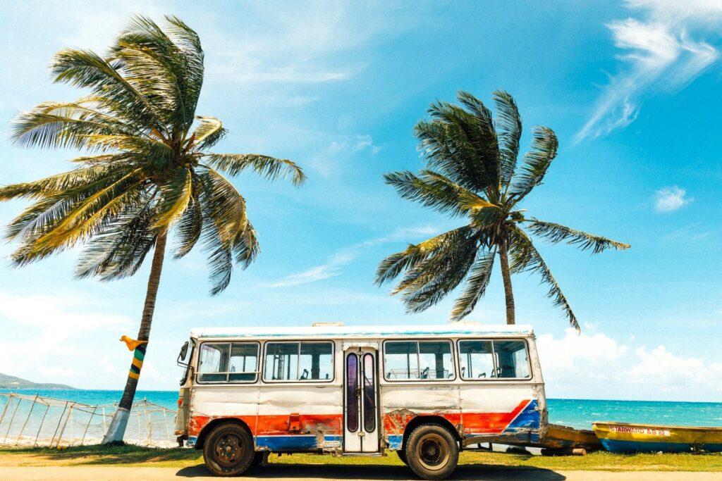 A typical beach in jamaica with palmtrees, boats and a very old colorful bus