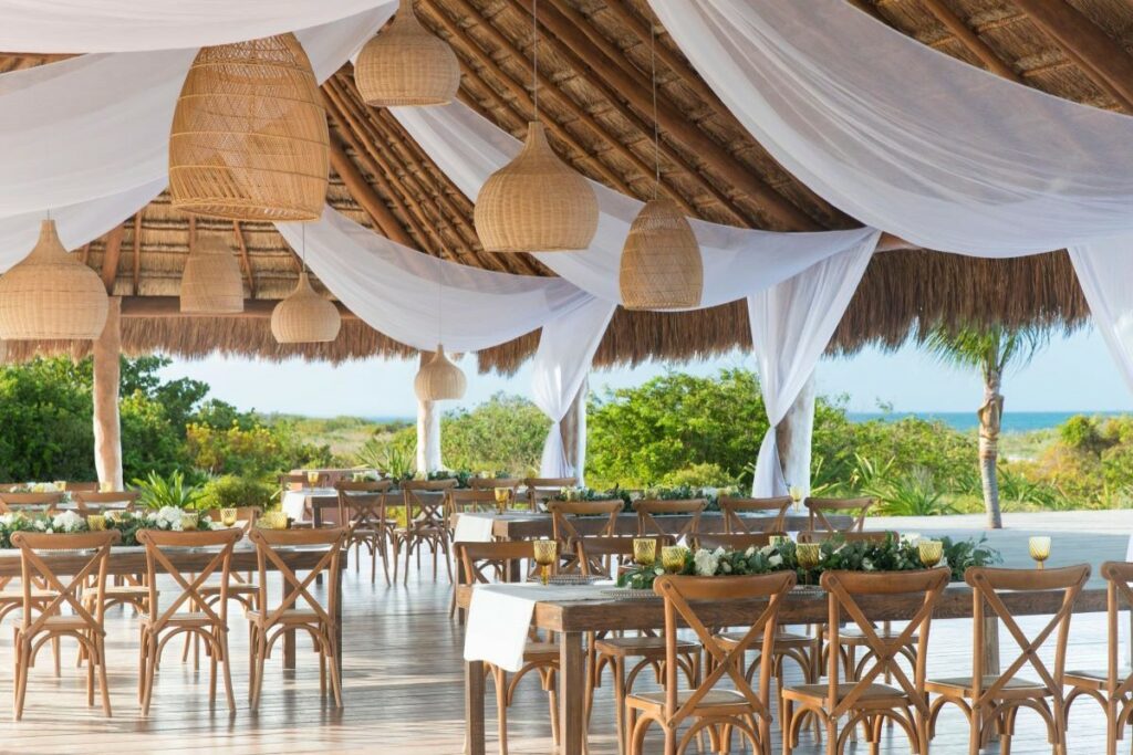 Wedding set up in an open palapa with hanging lanterns, drapes and modern wooden furniture
