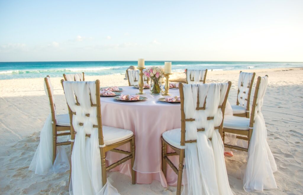 beach wedding reception set up with golden chairs, white drapes and pink accents