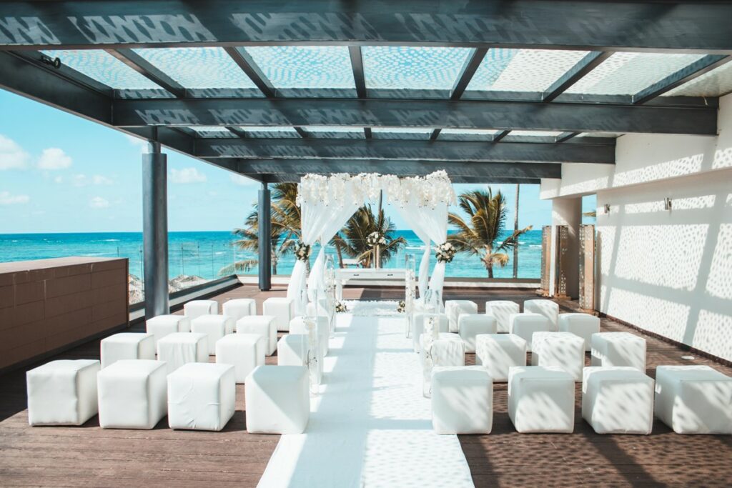 Royalton bavaro Sky Terrace wedding ceremony with white cube chairs, and white drapes over wooden pergola