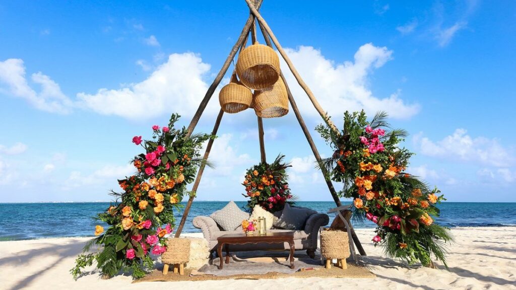 Gorgeous teepee at the beach decorated with flowers and white furniture for a couple to sit.