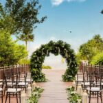 a beautiful wedding ceremony set up with a round arch with flowers on a deck in front of the beach