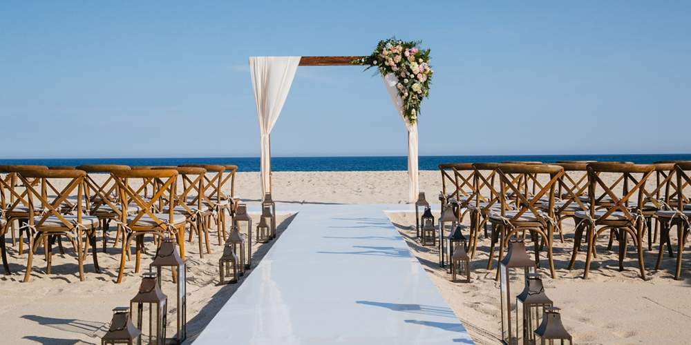 beach wedding set up with wooden chairs and an arch with flowers