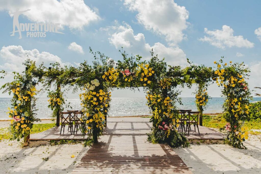 beautiful wedding pergola on the beach with lots of flowers and greenery